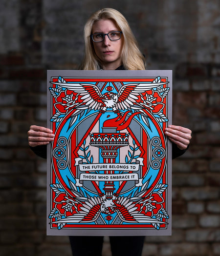 Lisa Champ of Red Halftone holding a limited edition print with a design of eagles and text against a brick wall.