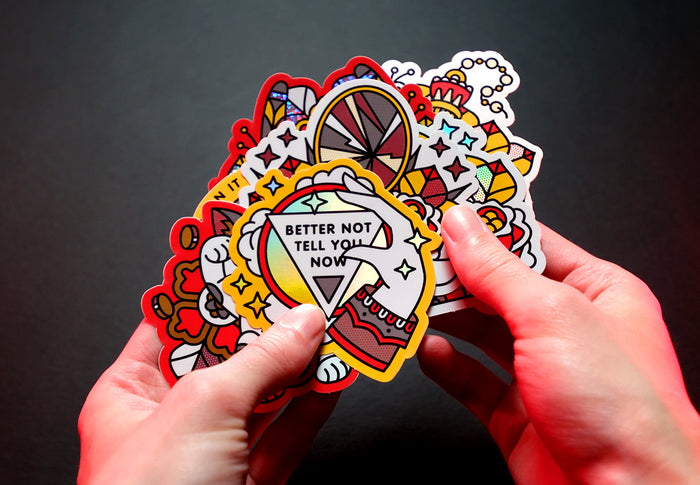 A bunch of colorful luck-themed stickers with text held by hands against a dark background