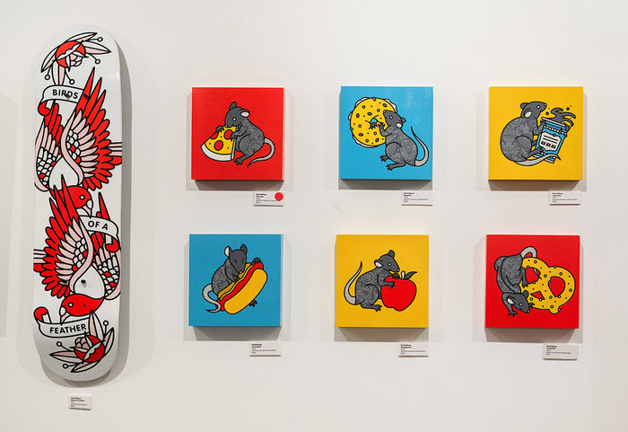 Original artworks by Red Halftone featuring a skateboard deck and colorful rat-themed paintings on a white wall