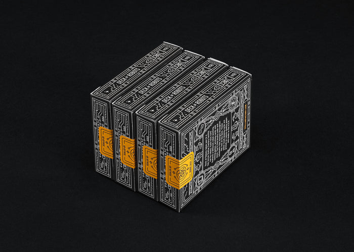 Four stacked playing card boxes with intricate designs and yellow labels on a black background