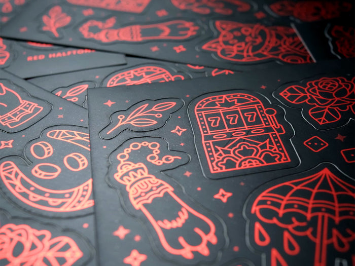 A close-up of a black sticker sheet with luck-themed red line art designs 