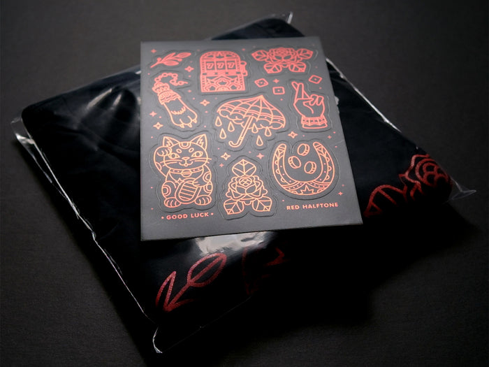 A black and red luck-themed sticker sheet on top of a folded black t-short on a dark background