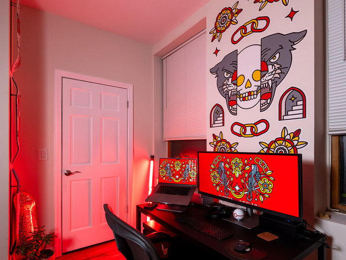 Modern home office with a desk featuring two computer monitors, a laptop, and decorative wall art in a red theme.