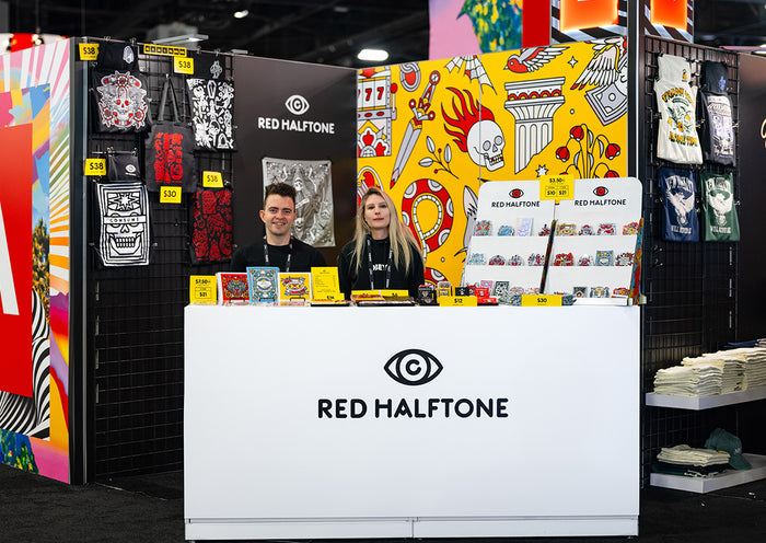 Lisa Champ of Red Halftone at her booth at Adobe Max in Miami, FL, with colorful merchandise and a person behind a counter.