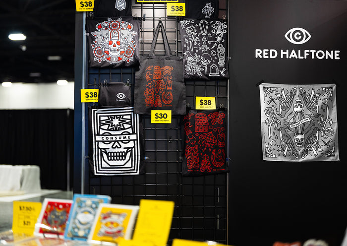 Display of graphic t-shirts with various designs on a black wall, featuring the brand 'Red Halftone' at Adbe MAX in Miami, FL.