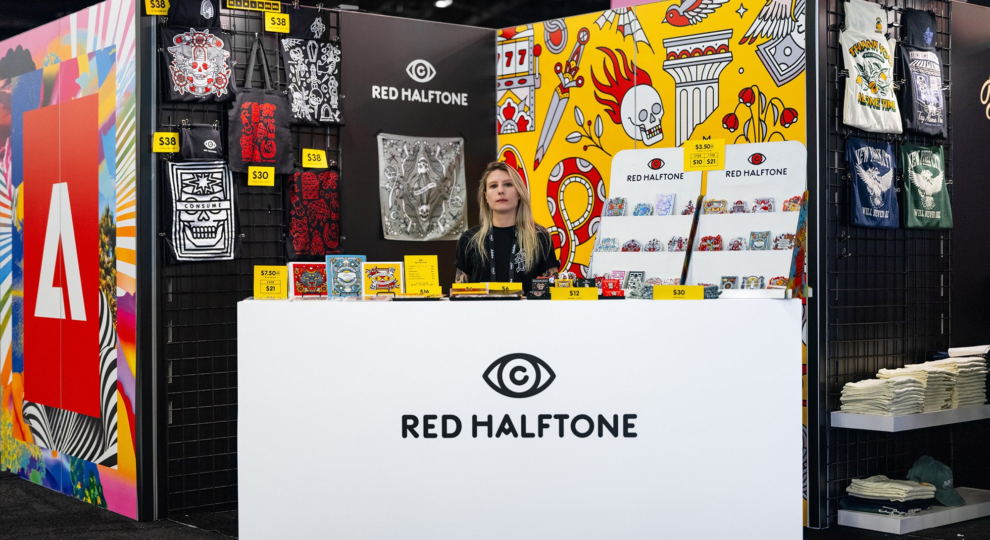 Lisa Champ of Red Halftone at her booth at Adobe Max in Miami, FL, with colorful merchandise and a person behind a counter.