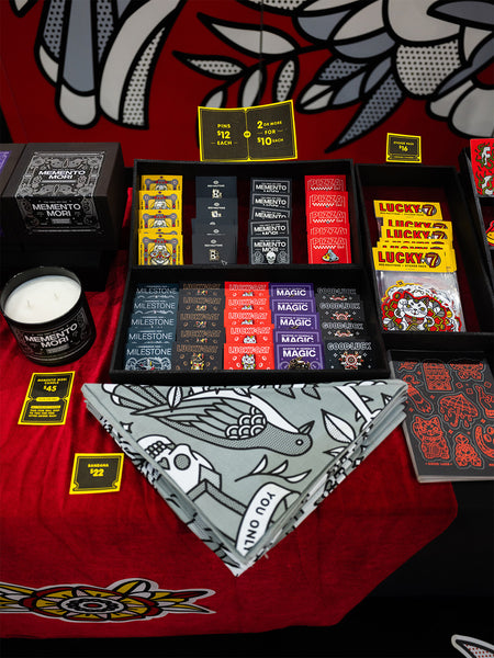 Collection of Red Halftone pins, sticker packs, bandanas and a candle on a red velvet surface.