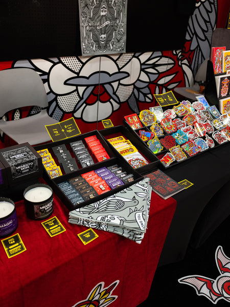 Table with various Red Halftone products, including stickers, pins, and candles, with a colorful and branded background.