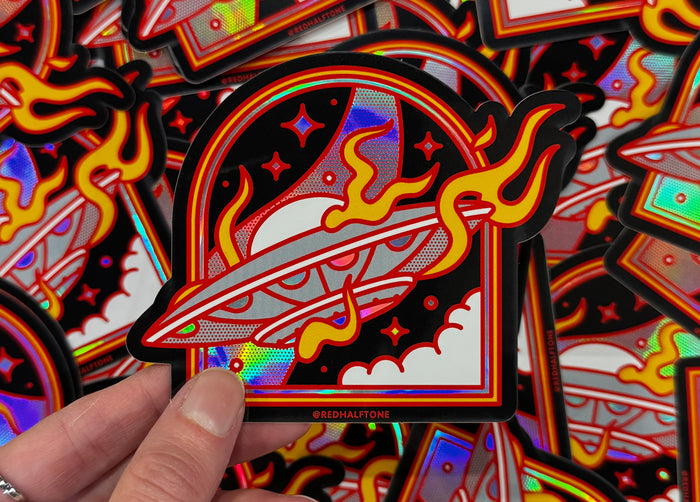Colorful holographic sticker with a spaceship design held by a hand against a background of similar stickers.