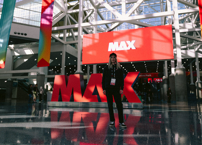 Lisa Champ of Red Halftone  standing in front of a large 'MAX' sign inside a building with a modern architectural design at Adobe MAX, Los Angeles.