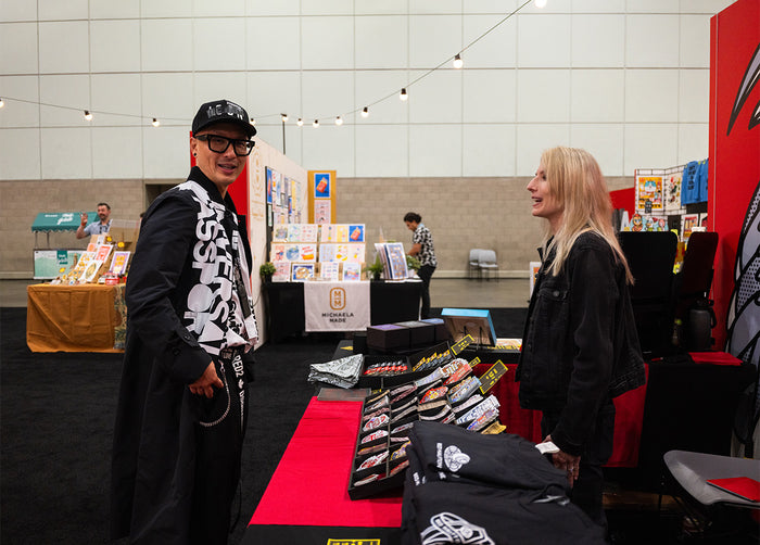 Chris Do and Lisa Champ of Red Halftone  interacting at Red Halftone's booth with merchandise display at Adobe MAX