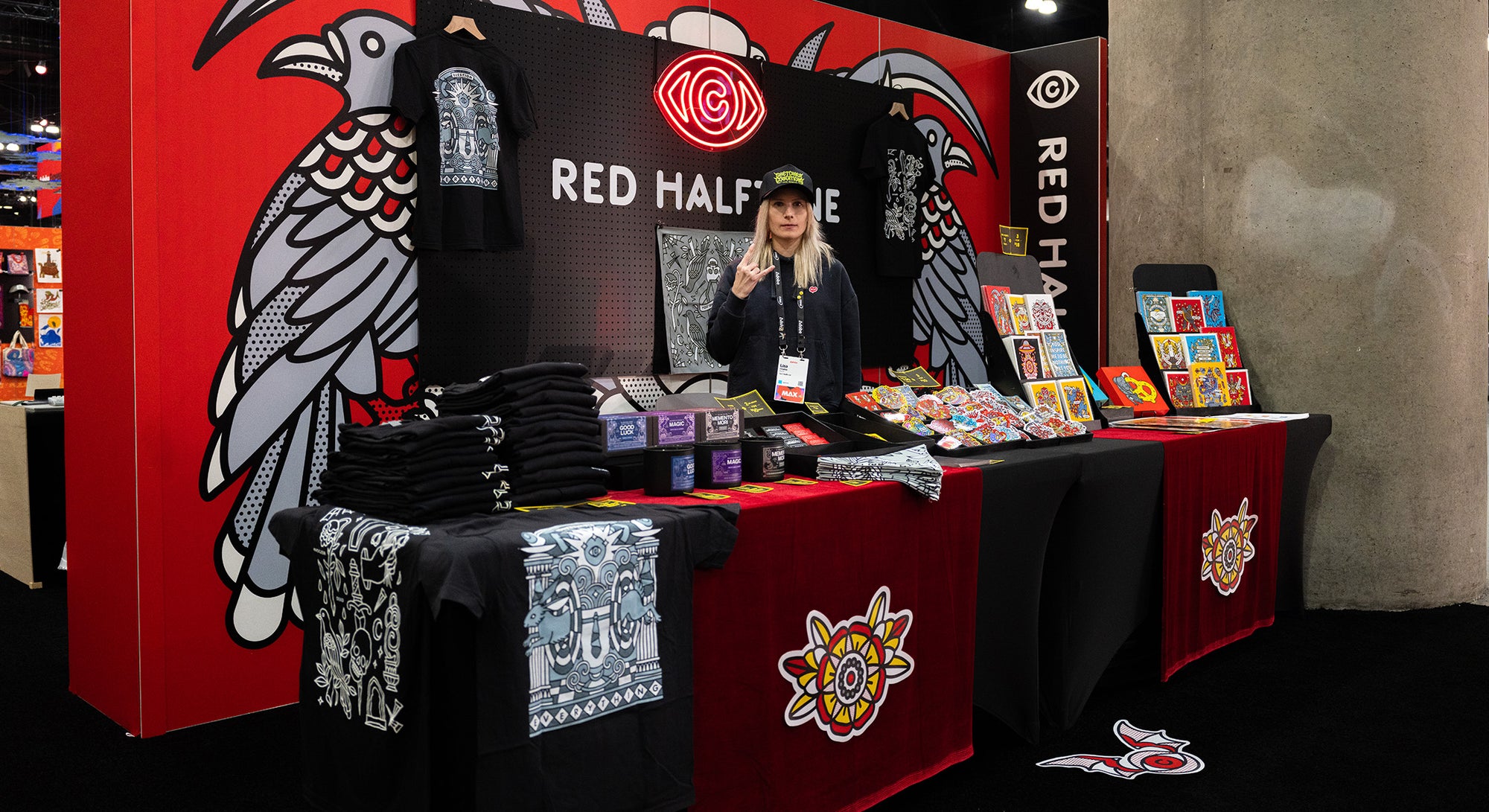 Lisa Champ of Red Halftone at Adobe MAX in Los Angeles, standing at her art and merchandise booth.