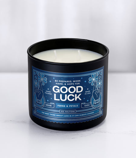 'Good Luck' Red Halftone Candle in a black glass jar with a blue label on a white background