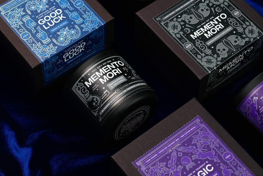 Collection of ornate candle packaging with 'Memento Mori' and 'Good Luck' text on a dark background.