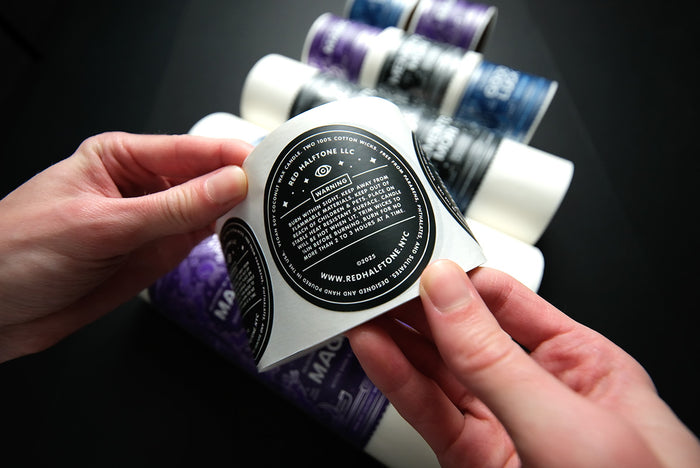 Person holding a roll of black circular warning labels against a dark background