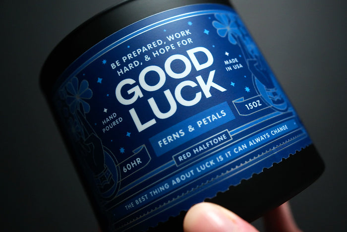 Blue label on a candle with text and floral designs, held against a dark background.