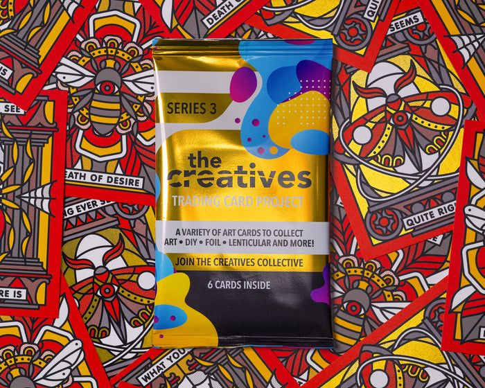 A foil pack of trading cards by 'the creatives' trading card project on a bunch of colorful trading cards.