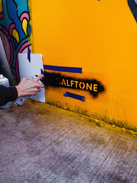 Artist Red Halftone using a stencil to pray paint her handle on the mural