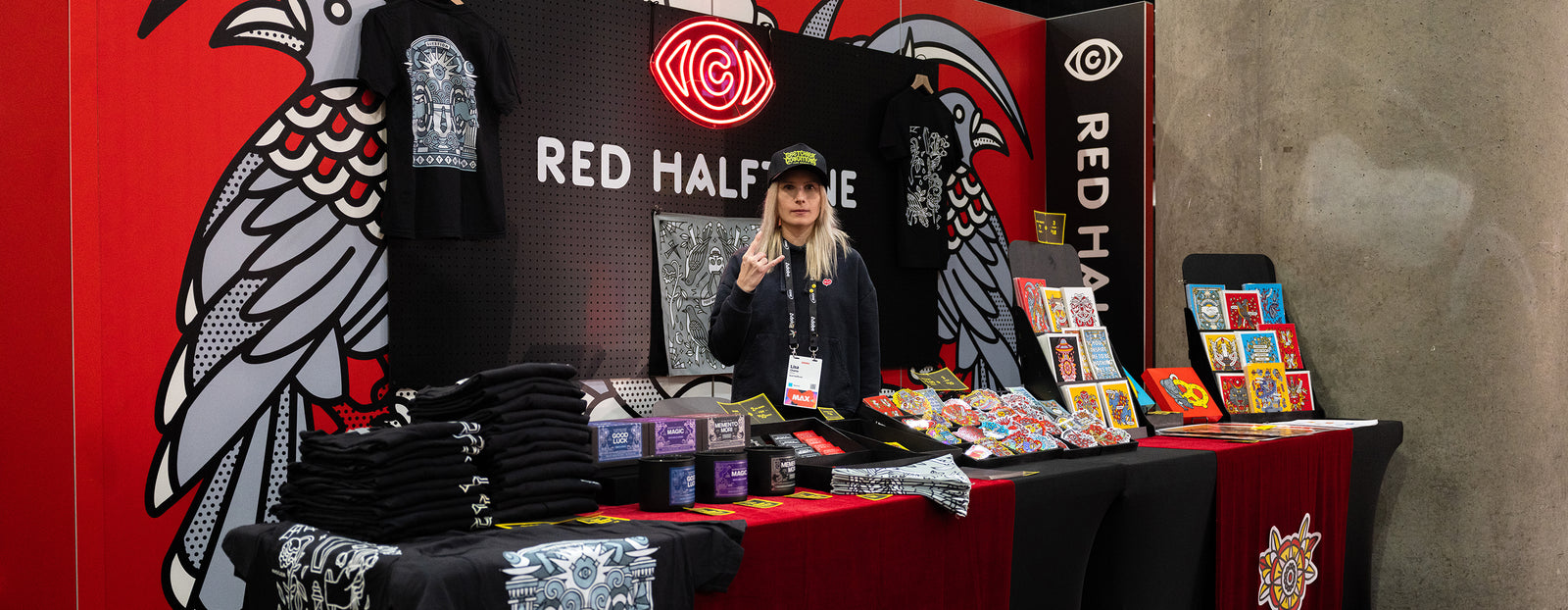 Lisa Champ of Red Halftone standing behind he booth with merchandise at Adobe MAX in Los Angeles.