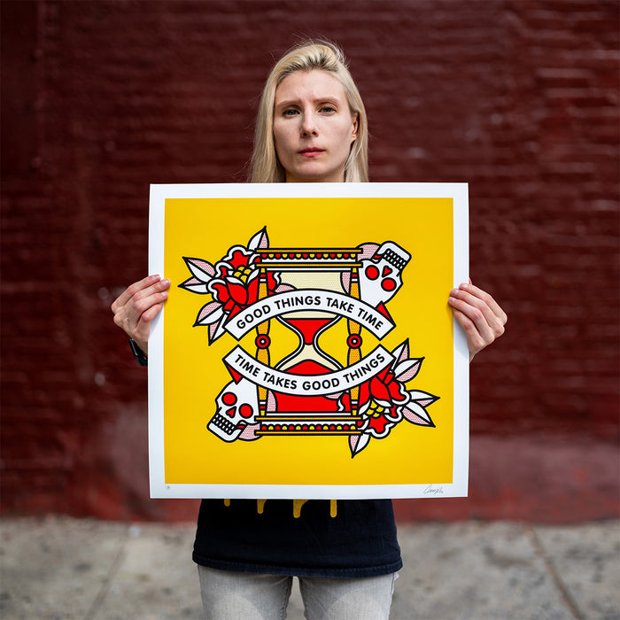 Lisa Champ of Red Halftone holding up a limited edition print. The design is of an hourglass surrounded by roses and skulls with the text "Good things take time, time takes good things".