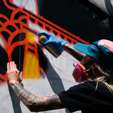 Lisa Champ of Red Halftone spray painting a red and black design on a wall.
