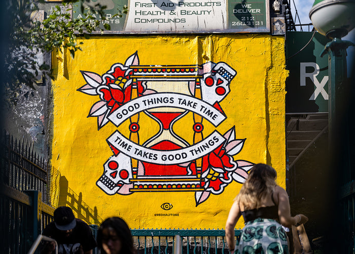 A mural by the artist Red Halftone on a building exterior in the Lower East Side of New York City. The design is of an hourglass surrounded by roses and skulls with the text "Good things take time, time takes good things".