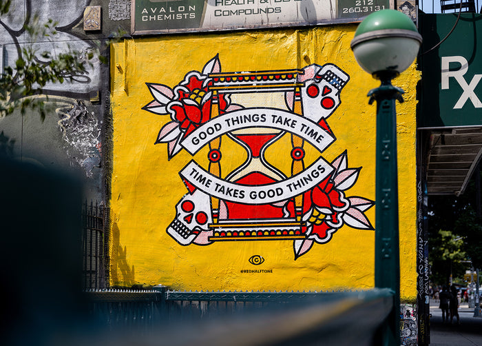 A mural by the artist Red Halftone on a building exterior in the Lower East Side of New York City. The design is of an hourglass surrounded by roses and skulls with the text "Good things take time, time takes good things".