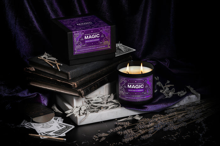Magoc candle and packaging by Red Halftone on a dark and purple velvet background with books, playing cards,and dried sage and lavender.
