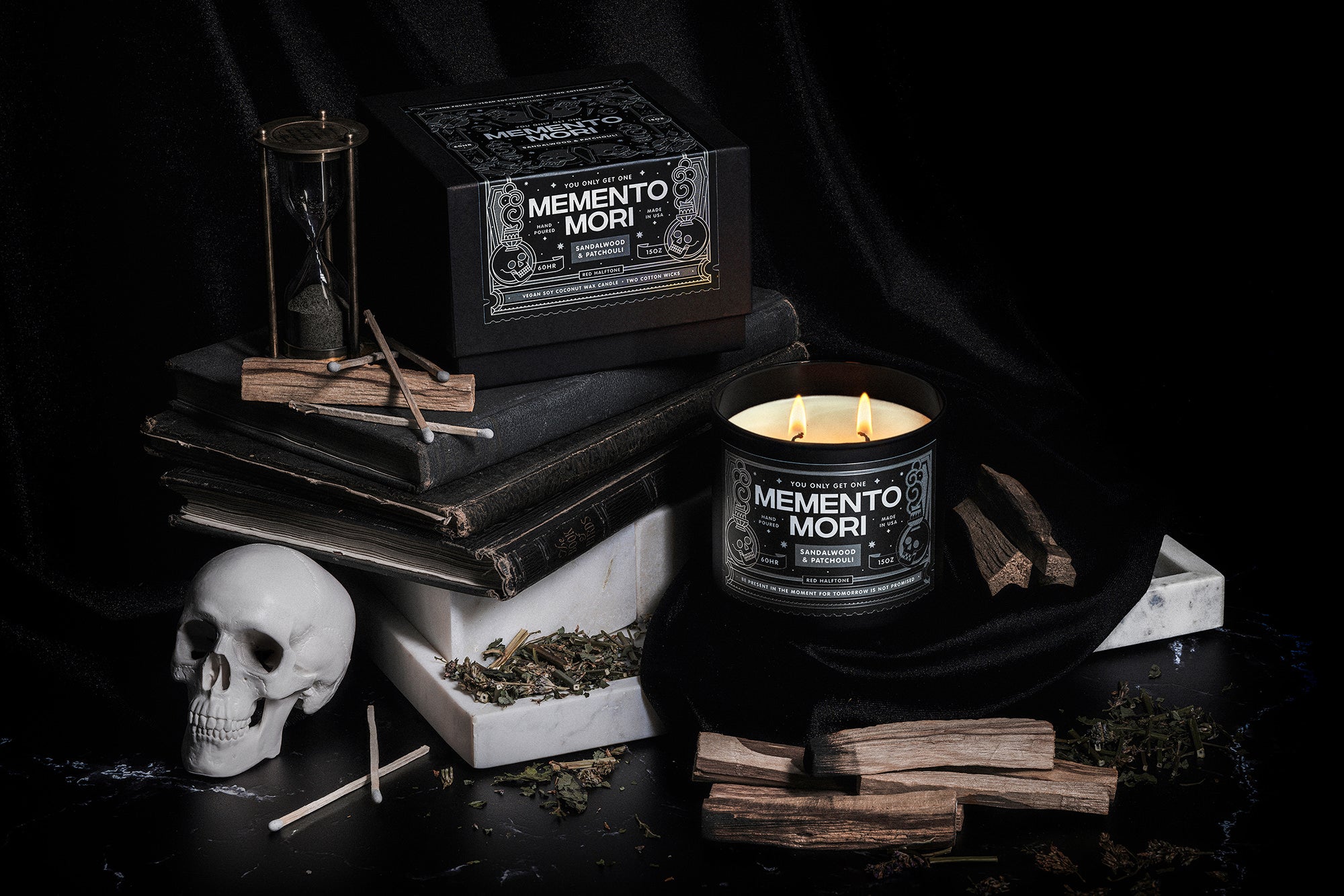 Memento Mori candle and packaging by Red Halftone on a dark background with books, skull, and other dark elements.