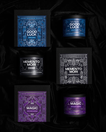 An overhead view of 3 candles with the boxes they come in arranged in a two by three grid on a dark velvet background.