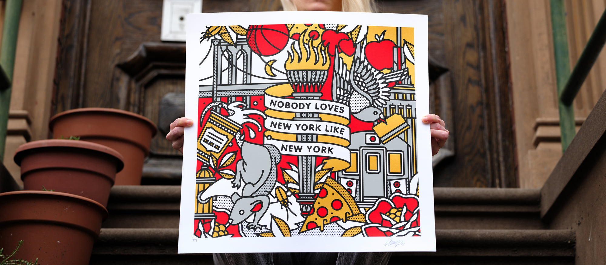 The artist Red Halftone holding a colorful limited edition screen print with New York-themed design against a on a stoop.