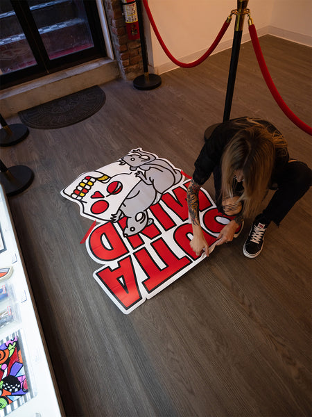 Red Halftone placing a colorful floor sticker graphic that says "Outta Mind" on a wooden floor.