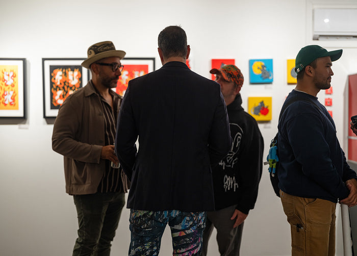 Four men standing in a gallery looking at colorful Red Halftone paintings on the wall.