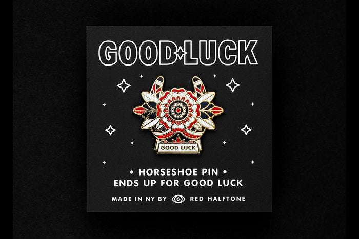 Enamel pin of a horseshoe and flower with 'Good Luck' text on a black background with stars.
