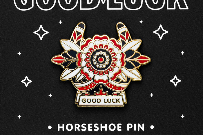 Enamel pin of a horseshoe and flower with 'Good Luck' text on a black background with stars.