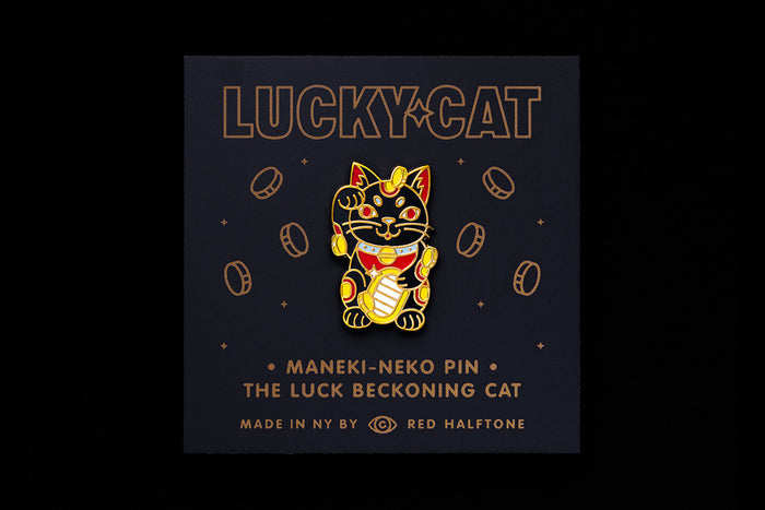 Maneki-neko enamel pin on a dark background with coins and text that reads "Lucky Cat"