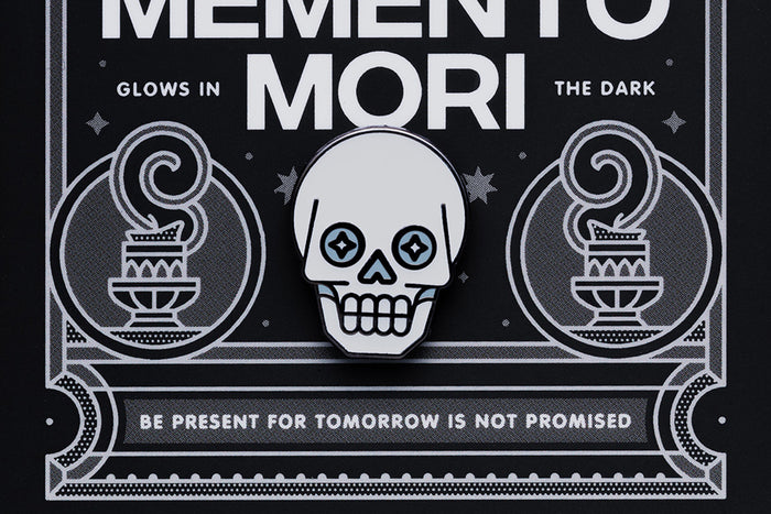 Skull enamel pin on a black card with text that reads "Memento Mori"