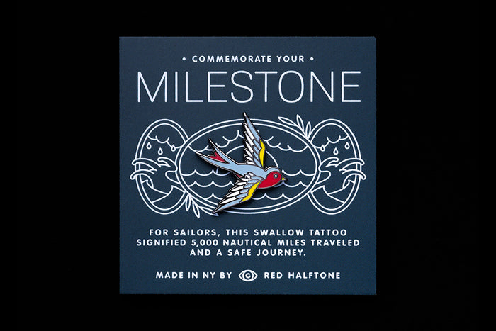 Enamel pin with swallow tattoo design on a dark blue background with text that reads "Milestone"