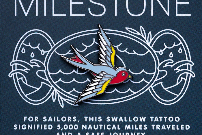 Enamel pin with swallow tattoo design on a dark blue background