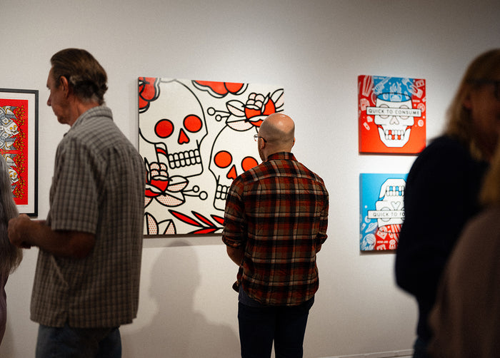 People viewing artwork by Red Halftone featuring stylized skulls on a wall.