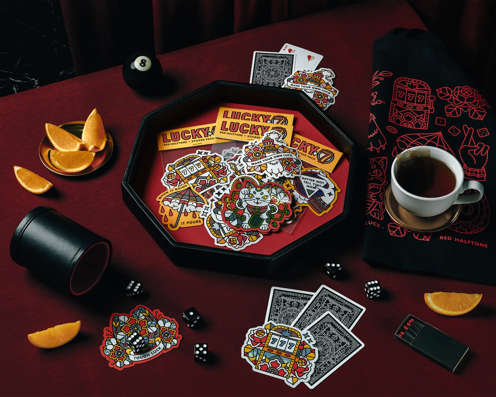 Lucky 7 sticker packs on a red velvet surface surrounded by playing cards, dice, oranges and other luck themed items.