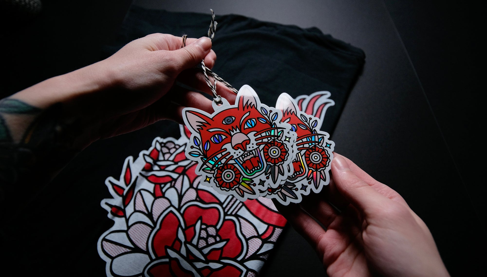 Person holding a hang tag of a colorful tiger design against a dark background