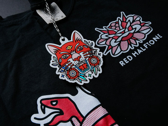 A hang tag of a colorful tiger design against a black t-shirt with red and white graphics