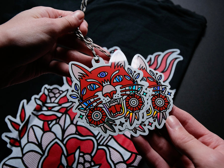 Person holding a hang tag of a colorful tiger design against a dark background