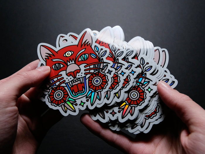 Hand holding a stack of colorful tattoo-style stickers with a fierce tiger design on a dark background.