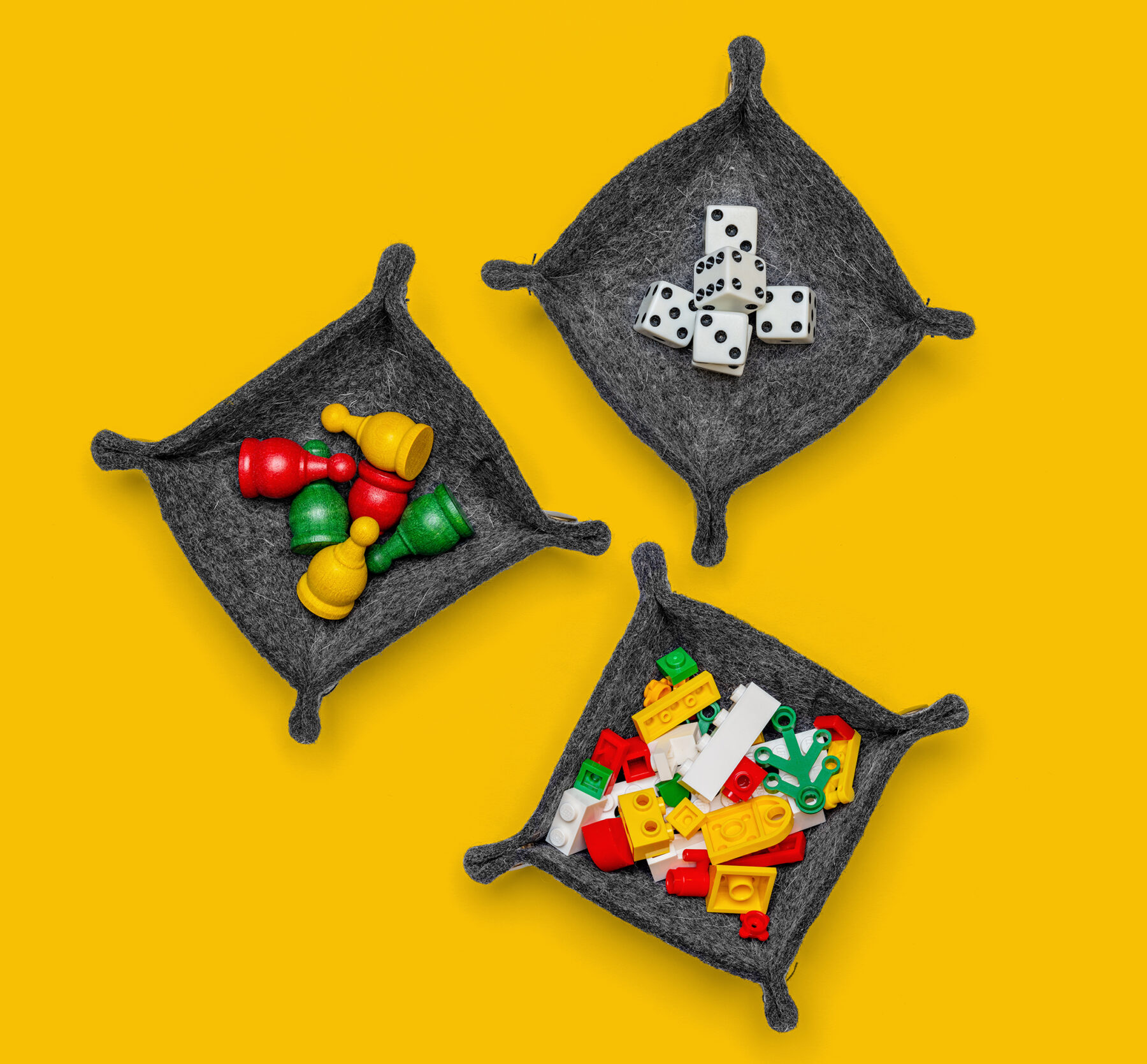 A birdseye view of three assembed trays each one holding: dice, colorful pawns, and Lego pieces.